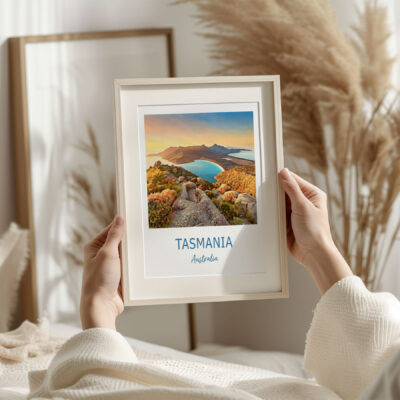 Person holding framed Tasmania photo in cozy room.