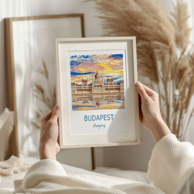 Hands holding framed Budapest artwork on bed