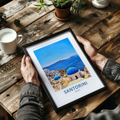 Person holding framed Santorini painting on table.